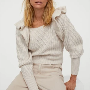 NY kabelstickad tröja med volang från H&M - Säljare står för frakt! Helt ny och oanvänd kabelstickad tröja! (Nypris 299kr) Etiketten sitter kvar! Mjuk kvalitet, vid ärm ribbstickad vid ärmslut ich nederkant.  Material: Ull - 6% Akryl - 30% Polyester - 64%