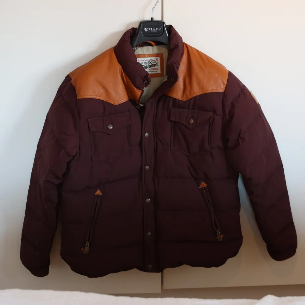 Vinröd dunjacka från Penfield i trailerwear-stil. Läderdetaljer i beige.  Den är mycket sparsamt använd men har fått en liten skavank på vänster axel. . Jackor.