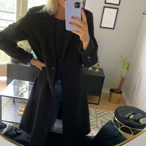 Lång svart kappa från H&M - Lång svart kappa från H&M. Kappan har både knappar och band i midjan. Storlek 42. Sparsamt använd.