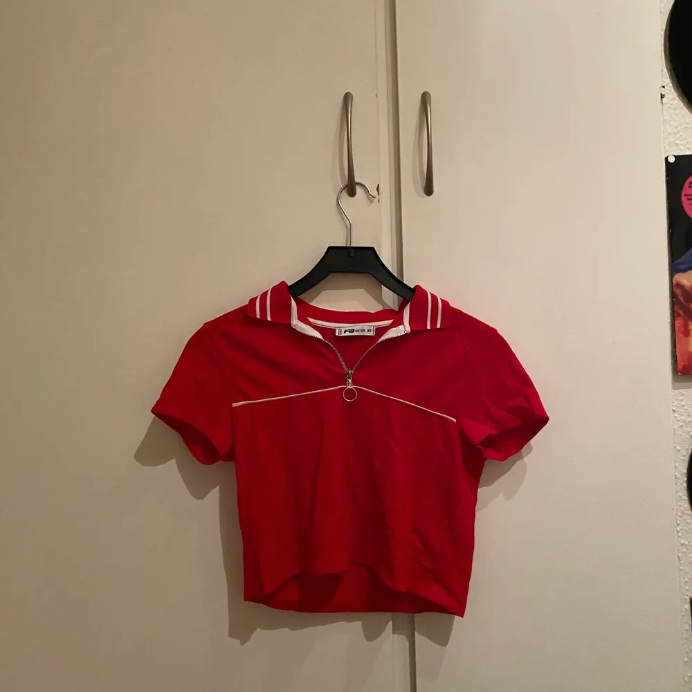 En croppad röd tröja, piké. Det finns en dragkedja på kragen som man kan reglera. Köparen står för pris+frakt🥰. T-shirts.