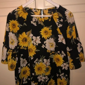 Blommig blus - En svart blus med gula solrosor på, storlek 40 med volang på armen 