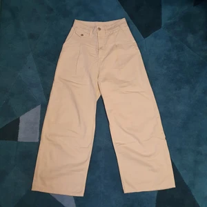 Beige byxor från Monki - Vida beige byxor från monki. Croppade på mig som är ca. 165. Strl. 32 (Jag brukar ha 34-36 i vanliga fall så passar definitivt större). Jag har använt ett svart skärp till dem så de är slightly missfärgade uppe där det ska sitta, (se bild 2 och 3). Om du har fler frågor kring t.ex mått så skriv :-) 