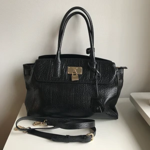 DKNY Väska  - DKNY handväska i svart skinn med gulddetaljer. Ganska så stor, man får plats med mycket i den! Sparsamt använd, med några skråmor på märket fram. Kommer med ett avtagbart axelband. Kan mötas upp i Stockholm. 