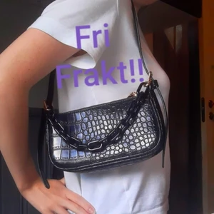 svart krokodilmönstrad väska  - Svart liten väska från JFR med gulddetaljer💖Kan bäras i sin kedja eller över axeln med det avtagbara/reglerbara axelbandet som medföljer(Bild1). Bild 2 från JFR's hemsida som visar när man bär den i kedjan. Mått: bredd: 22cm, höjd: 12cm Fint skick!💖Bjuder på frakten!