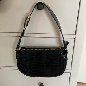 Svart väska  - Svart axelväska i ”ormmönster” och gulddetaljer. Använd ett fåtal gånger, så den är i fint skick. Fin och rymling, men kommer tyvärr inte till användning. Köparen står för frakten! Hör av dig vid frågor eller fler bilder! ❤️