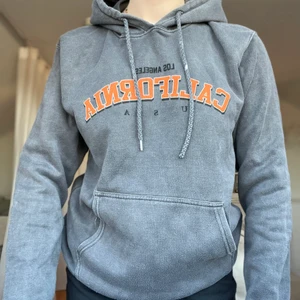 Hoodie - En hoddie i en urtvättad grå färg med orange tryck ifrån boohoo det är en S men ganska stor i storleken. Jag får en retor känsla av denna tröja vilket jag tycker är snyggt 