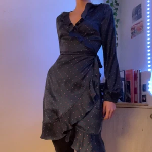VERO MODA sidenomlottklännings  - Säljer denna jättefina marinblå satin omlottkslänning med gulliga rosa prickar, från vero moda. Klänningen är i fint skick och har använts bara ett fåtal gånger. Jag är 177 cm.