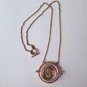 Halsband Timeturner Harry Potter - Hermiones timeturner halsband från Harry Potter böckerna/filmerna. Blank som guld men lite mer åt det kopparfärgade hållet. De två inre cirklarna går att snurra, timglaset har sand som rör sig och text går runt de två yttre cirklarna. Kedjan är 56 cm lång så smycket ligger perfekt mot bröstkorgen. Kan frakta eller mötas upp i Stockholm:)