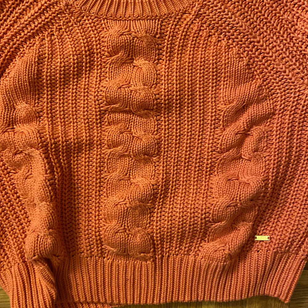 En rosa stickad tröja. Stickade detaljer på framsidan av tröjan.. Stickat.