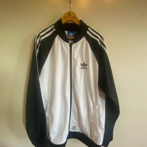 Ovanlig Track jacket från Adidas Originals i vitt med svarta ärmar och vita klassiska revärerna längs dem. På baksidan är det en björn med 👑 Herrmodell i storlek M. Köpt i USA för några år sedan för 800kr och den är knappt använd