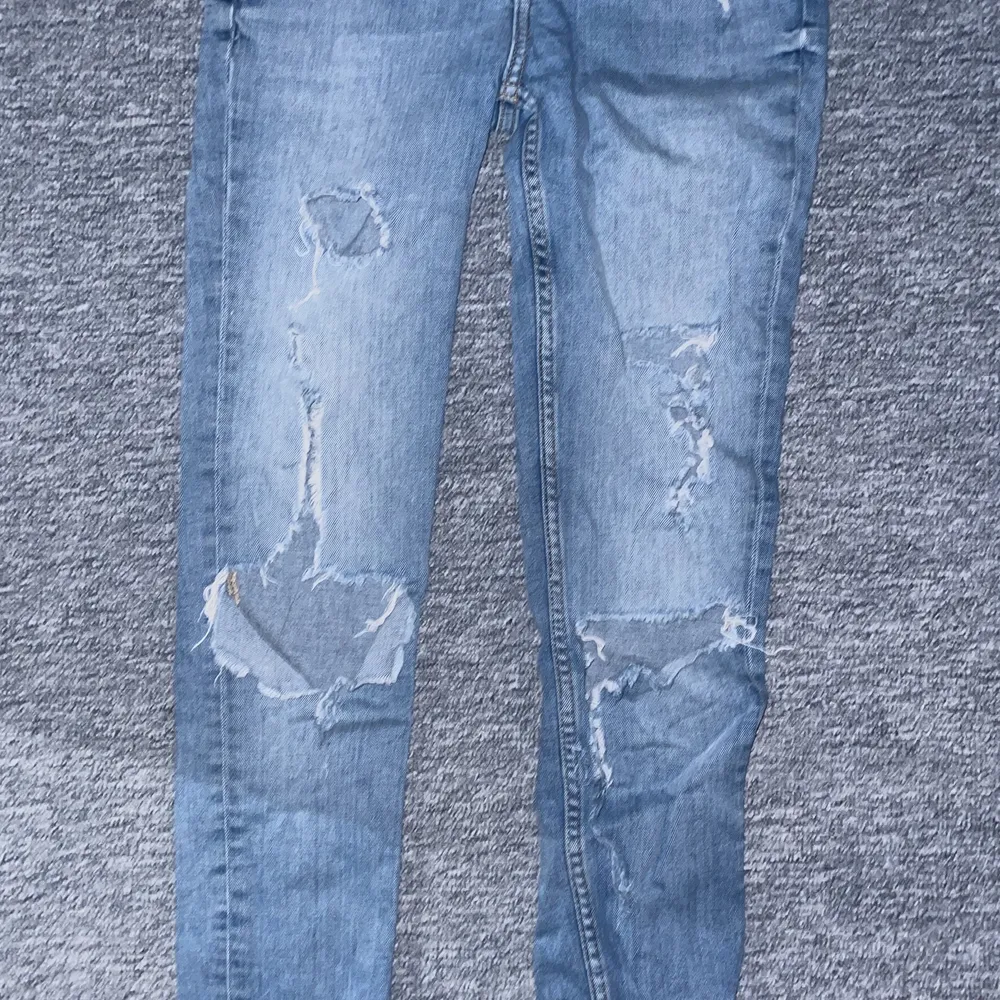 Ett par blåa jeans med hål på knäna å även hål i fickorna ibak. Storlek 26. Använda ganska mycket . Jeans & Byxor.