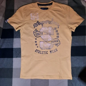 Superdry Tshirt strl S - Superdry tshirt i tjock bomull med urtrvättat tryck på. Osäker på om det är damstorlek men den är märkt strl S och längden är ca. 70cm. Kan hämtas i Hammarby Sjöstad, annars står köpare för frakten :)