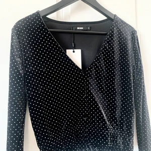 Blus med metalldots - Svart blus i sammet med små silvriga matta metalldots. Fin v-formad urringning med svarta sammetsknappar. Stretchig resår nedtill. Oanvänd. Från bikbok.