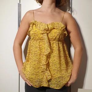 Chiffong topp, storlek M - Gult linne av chiffong med rosa blommönster. Har ett lager polyestertextil innanför chiffongmaterialet. Justerbara axelband. 