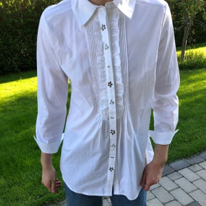 Vit skjorta - Vit skjorta med mönster vid knapparna. 77 cm lång/ 44-45 cm bred. Storlek EU 42 vilken jag antar är en L/XL. Jag är 182 cm lång och väger 73 kg.