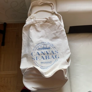 Sjömanssäck - Snygg säck, mjölk- färg, bomull 100%, praktisk med snöre uppe och ett rem på sidan längst hela säcken, inga fläckar, nyskick, rymlig.