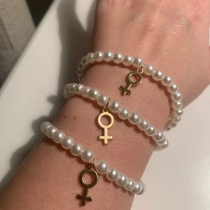 Elastiskt pärlarmband med kvinnosymbol - Elastiskt pärlarmband med guldpläterad kvinnosymbol. 17cm och passar de flesta vuxna handleder .