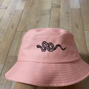 Detta bucket hat är inte gammal. Den har aldrig varit använt. Det är en rosa bucket hat med en svart orm. Materialet är jätte bra.