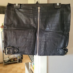 Bikerkjol - Svart bikerkjol i skinnimitation med dragkedja och spännen. Knappt använd. Storlek 38. Rök- och djurfritt hem. Kan skickas mot fraktkostnad!