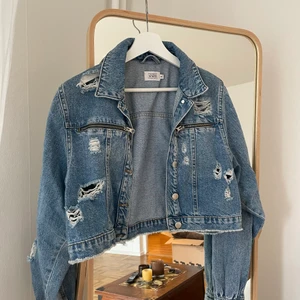 Kort jeansjacka från influencerkollektio - Sliten kort jeansjacka från Donna Rominas kollektion för NAKD. Strl 40 men passar mig som är 36.