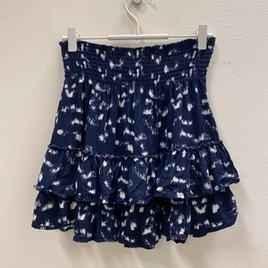 Kort mönstrad kjol  - Kort kjol i blått med vitt mönster. Volanger nertill och smockat tyg upptill. Sååå fin på. Tyvärr för liten för mig.. Storlek 38 men mer som en 34-36. fler bilder kan tas vid önskemål. Frakt tillkommer 