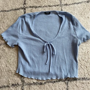 Blå v-ringad topp  - Denna fina toppen är bra kavlitet, nästan lite stickad men luftigt material. Den är inte så jätte v-ringad. Knuten på framsidan går inte att justera själv. Material justeras efter din kroppsform och är väldigt stretchig