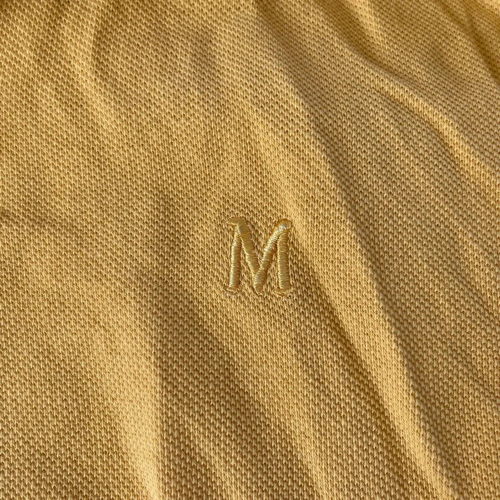 Gul polo T-shirt med två svarta ränder på ärmarna och markerade sömmar, ett broderat M på bröstet. 20kr+frakt. T-shirts.