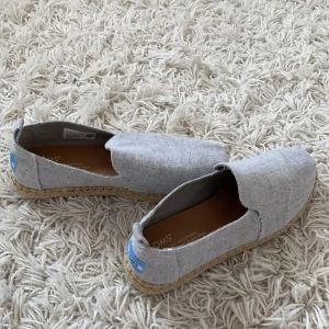TOMS skor - Stått i garderoben och är helt oanvända. TOMS skorna är  ljusgråa och materialet är linneaktigt så passar perfekt till sommaren med lite luftigt tyg. Säljer pga inte min stil