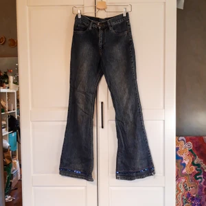 Utsvängda Lee jeans med cool detalj - Behöver tyvärr sälja dom här för att de är alldeles för små för mig. Ett par jätteschyssta Lee jeans med utsvängda ben och låg midja, paljettdetaljer längst ner på byxbenen. Fint skick. Minimala slitningar längst ner på benen som syns på bilden med paljetterna. Mått: 68 cm midja 78 cm insida benet (från skrev till fåll) 26 cm rise (från skrev till midja). Står inte material i men gissar 100% bomull (0 stretch)