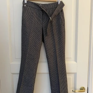 Kostymbyxor i ullblandning - Kostymbyxor från Björn Borg i ullblandning och hundtandsmönster(?) i en rak modell. Storlek 34 men ingen stretch så kan upplevas lite liten. Gylf med dragkedja och knapp. Ett skärp med metallspänne på vänstersidan. Material: 45% ull, 55% polyester. 