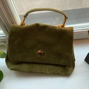 Liya suede handväska, coccinelle -  Helt oanvänd handväska från coccinelle som mamma ej har intresse för. Fodralet finns fortfarnde från köpet. Skicket är nytt och perfekt med inga negativa detaljer alls. Namnet på väskan är Liya Suede handbag (moss green) och kostar nypris 3800kr. 
