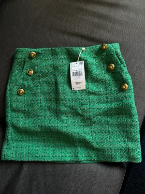 Grön tweedkjol guldknappar - Helt oanvänd med prislappen kvar, köpt i Spanien. Strl S i bomull, polyester och viskos.   Dragkedja bak och två fickor fram.