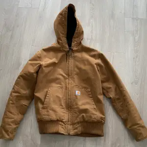 Carhartt J130-M  Storlek S passar M. Armhåla till armhåla - 61cm, Axel till nedre del av jackan - 70cm, Armlängd - 68cm, Färg: Carhartt Brown   Info: Nyskick knappt använd. Liten smutsfläck på vänster arm men kan förmodligen tvättas bort. 