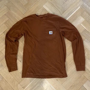 Carharrt long-sleeve shirt - Denna tröjan är väldigt snygg med ett litet hål vid bröstfickan och några små flöckar som kan lätt tvättas bort.