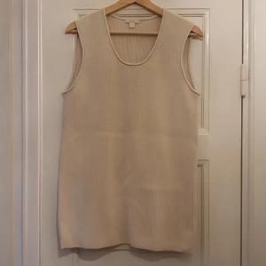Stickad väst från COS - En längre väst i krämvitt/beige.  64% bomull 36% polyamid. Längd 72 cm.