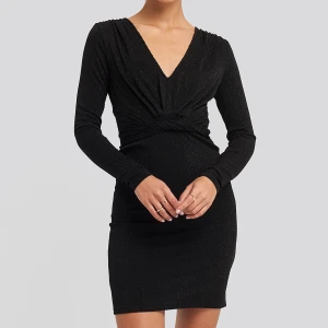 Glittrig klänning  - Svartglittrig långärmad klänning med knutdetalj under byst. Kort och sitter tajt. Aldrig använd med prislapp kvar.