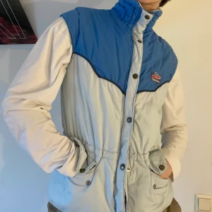 Vintage blå ljusblå dunväst 80s - Vintage dunväst i ljusblå och havsblå med snörning i midjan, fickor, texturerad logga på bröstet och det coolaste trycket på insidan ❄️⛷