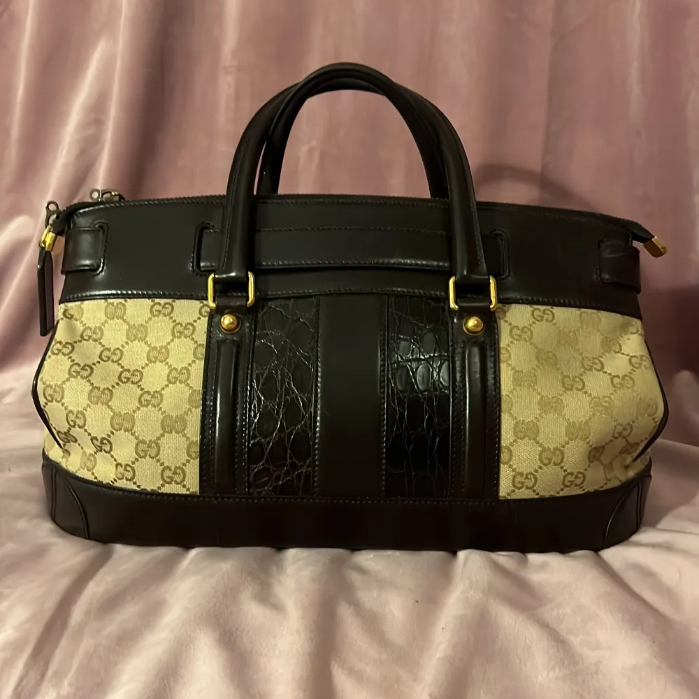 Äkta Gucci väska säljes. I nyskick, sparsamt använd. Inköpt i Marbella 2008, kvitto har inte sparats.  I läder, tyg och krokodil skinn. Bredd: 40cm, höjd: 20cm. Köpt för ca 18000 kronor.. Väskor.