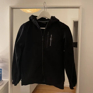 Svart Sail racing kofta  - Svart Sail racing kofta med luva i storleken 160. Kedja framtill och på bröstet. Har fickor. 