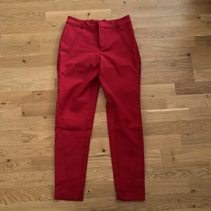 Kostymbyxor  - Röda figursydda kostymbyxor. Insydda i midjan, går att sprätta upp om man vill. Hund finns i hemmet. 