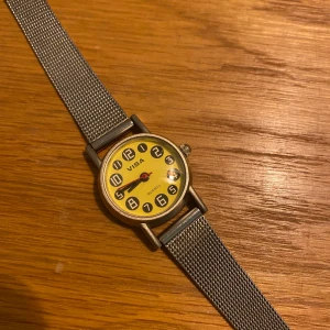 Klocka med armband i metall.  - Klocka av märket Quartz. Gul urtavla och armband i rostfri metall. Inga skador. Skick 9/10. Batteriet är nästan slut så det borde bytas snart. Klockan är ca 27 mm i diameter. 