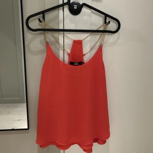 Bikbok linne med guldkedjor och öppen rygg - Linne från BikBok med guldiga kedjor och öppen rygg, sitter jättefint på. Somrig röd färg som ”poppar”. 