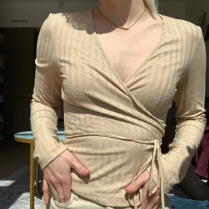 Beige omlott-tröja från NA-KD - Beige omlott-tröja i storlek 34 från NA-KD. Passar 34/36 eftersom man själv kan bestämma hur mycket man vill spänna in den. Fint tyg. Använd men i fint skick!