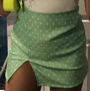 Grön prickig kjol  - Supersöt grön vit prickig minikjol köpt i Spanien strlk S. Har en slitning fram. Använd 1 gång så i helt nyskick. Kommer tyvärr inte till användning. 