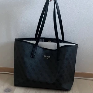 Guess väska - GUESS väska, bra skick, rymmer väldigt mycket! Färgen är en blandning av grå och svart. Pris kan diskuteras vid snabbaffär