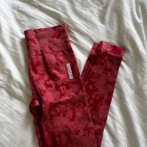Gymshark tights i röd färg med kamouflage-mönster, de är aldrig använda och helt nya. Lappen sitter inte kvar däremot. Storlek small. Köparen står för frakt!