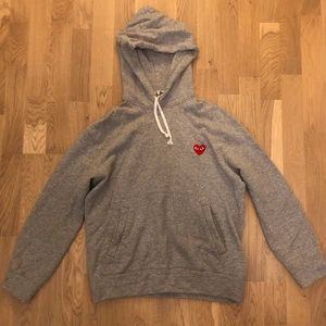 CDG Hoodie - Grå hoodie med broderat CDG Play hjärta på bröstet. Är i bra skick, lite använd. Hoodien ser ljusare ut i verkligheten, fick inte med den rätta färgen på bilderna men man ser på ett ungefär. Inga fläckar alls. Passar S/M, passar inte direkt L.
