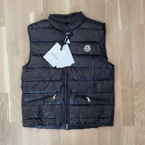 Moncler GUI Väst - En svart Moncler GUI Väst i färgen svart, NFC scan funkar på Moncler loggan och inutti västen. Kontakta mig vid yttligare frågor eller om fler bilder önskas :)