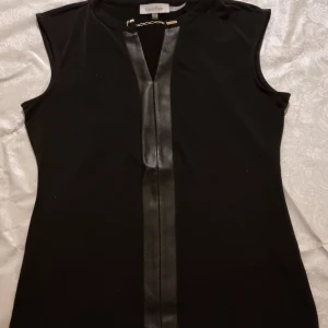 Calvin Klein Top - Svart top med kedja från Calvin Klein. Läderliknande detaljer. Kan användas både till vardags och fest. 