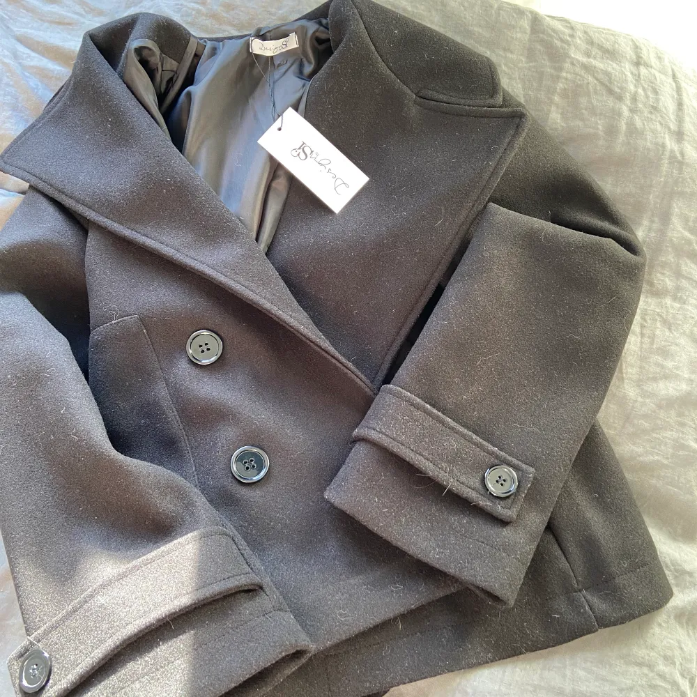 SÅLD!! Kort jättefin svart kappa från DesignBySi. Passar perfekt till vilken höstoutfit som helst! Helt ny, aldrig använd. Säljer eftersom jag har en liknande grå och inte behöver två stycken. Köpt för 799 kr, säljer för 600 kr + frakt 💞. Jackor.